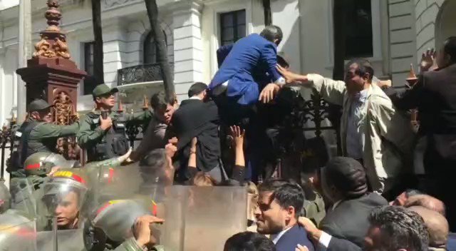 Guaido is trying to jump the fence to get into the National Assembly. He is being forcibly prevented by the GNB 