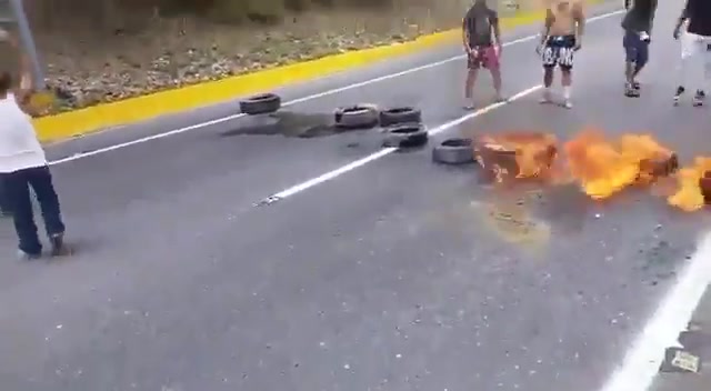 Angehörige der Nationalgarde (GNB) beobachten, wie Demonstranten auf der Autobahn Caracas – La Guaira Reifen anzünden.