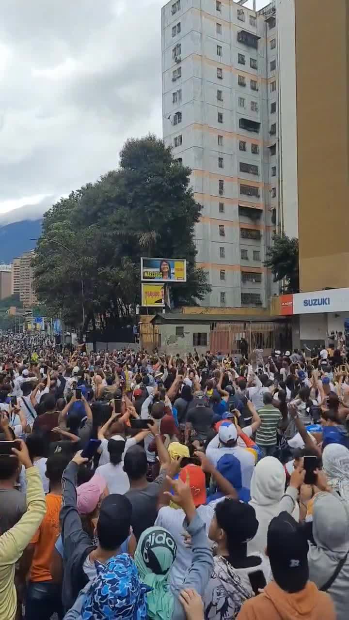 Protesters attempting to knock down a propaganda board by Maduro in La California