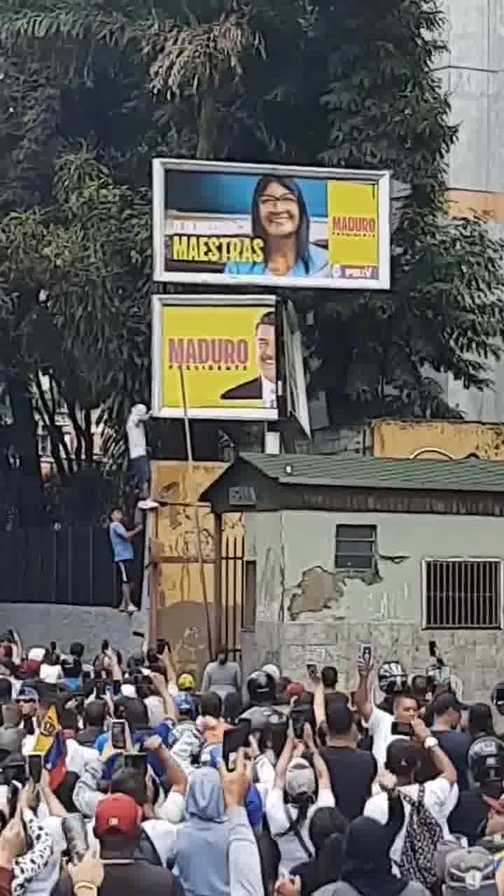 Demonstranten versuchen, in La California ein Propagandaschild von Maduro herunterzureißen.